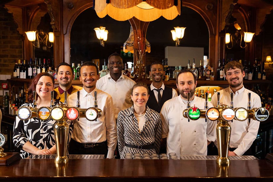 Team of bartenders and staff behind a bar with beer taps.